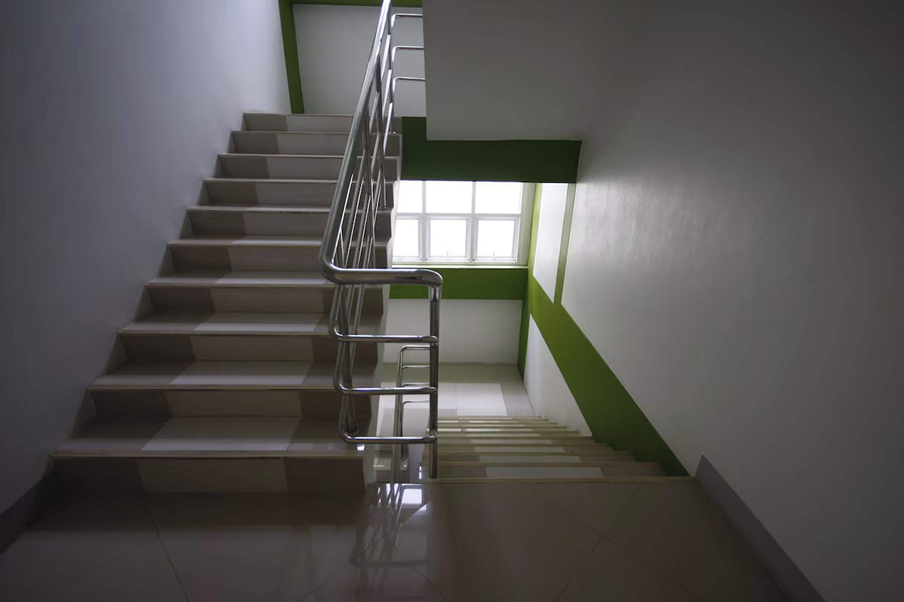 A staircase with a metal handrail, a window with a green frame, and a white wall.