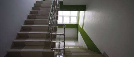 A staircase with a metal handrail, a window with a green frame, and a white wall.
