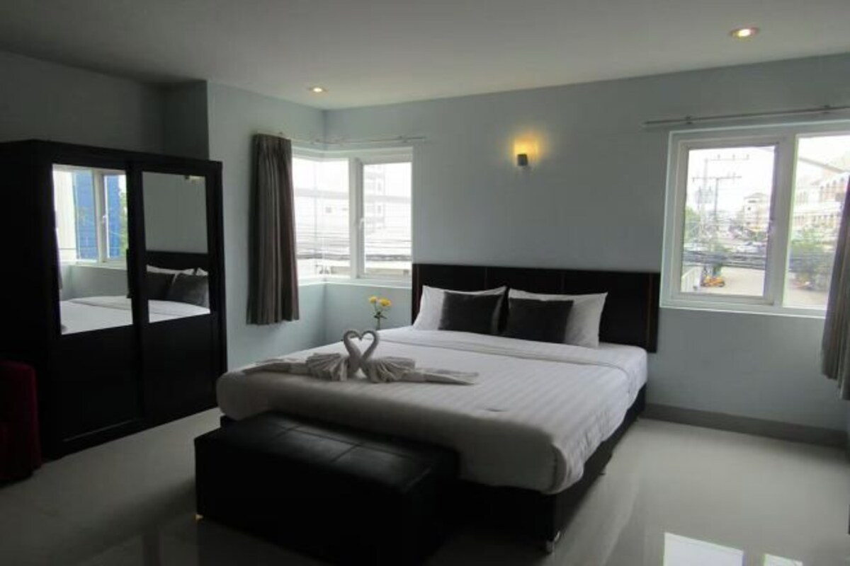 A modern hotel room with a large bed, a bedside table, a mirror, and a window with a view of the city.