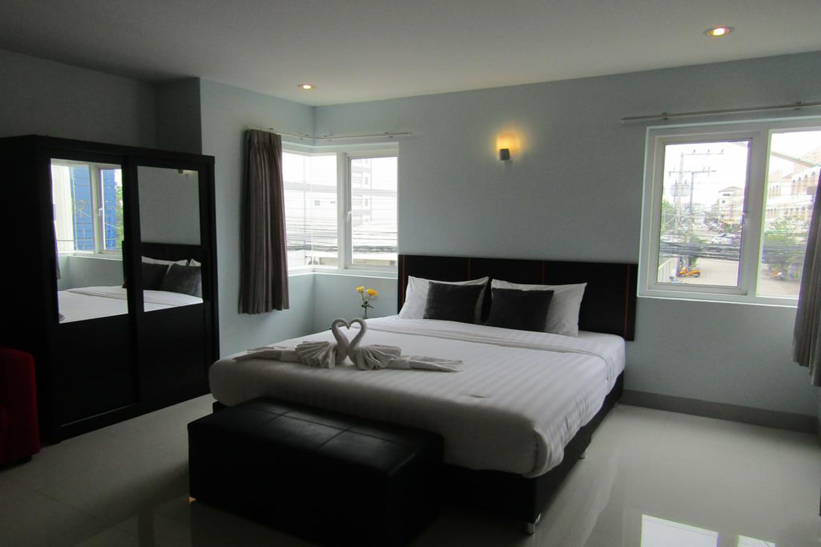 Habitación de hotel moderna con una cama grande, un espejo, un banco y vistas de la ciudad a través de las ventanas.