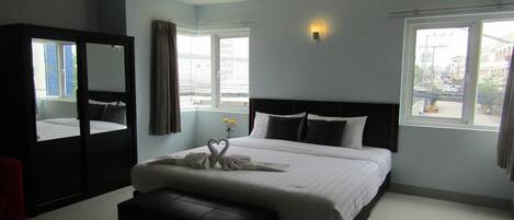 Habitación de hotel moderna con una cama grande, un espejo, un banco y vistas de la ciudad a través de las ventanas.