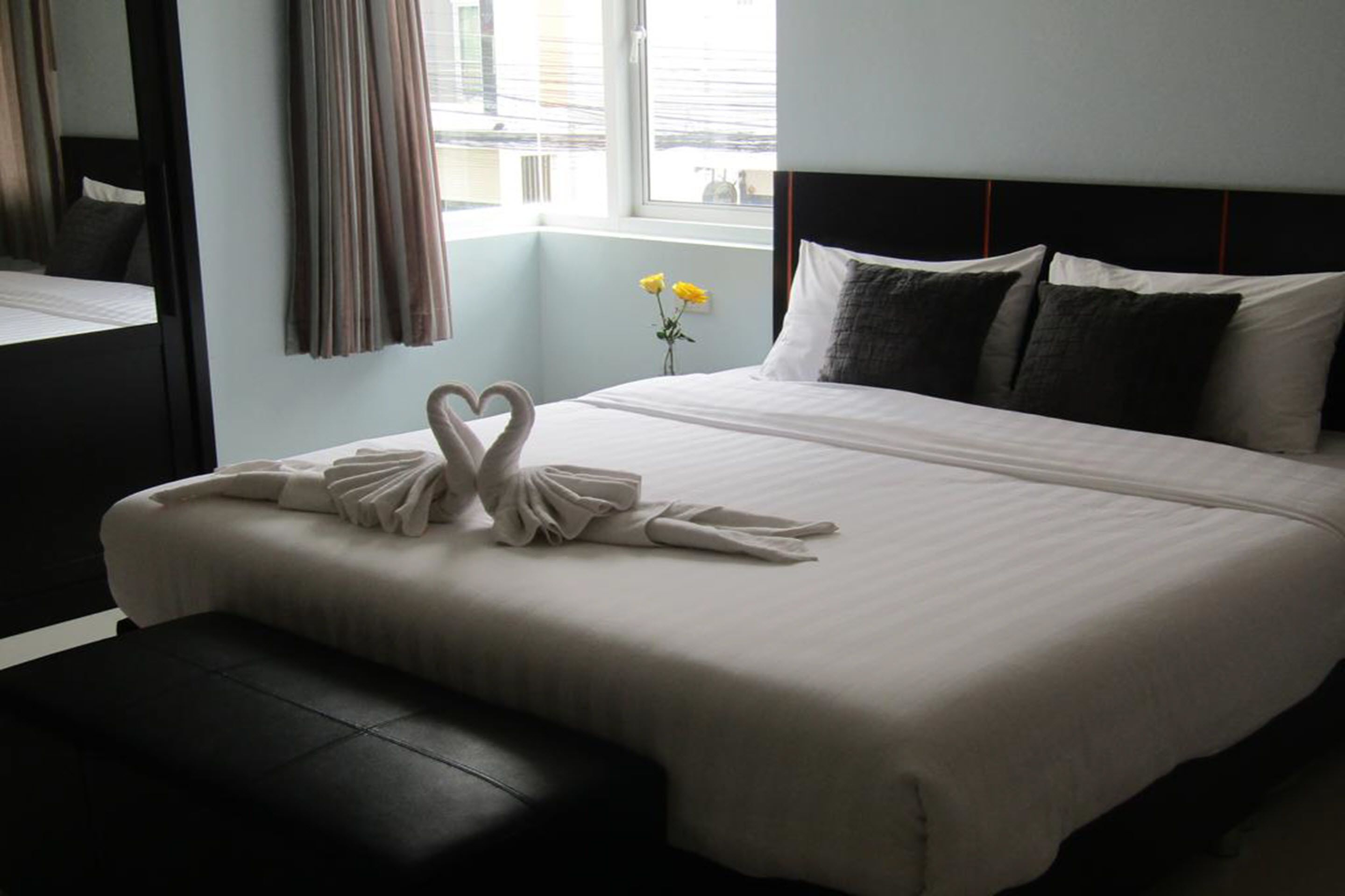 Una habitación de hotel con una cama grande, una mesita de noche, un espejo y una ventana con cortinas.