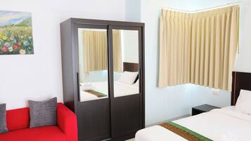 A hotel room with a bed, a red sofa, a wardrobe, and a painting on the wall.