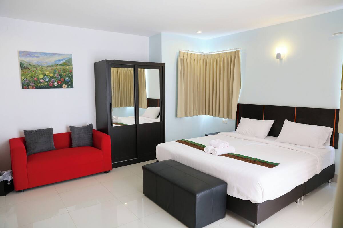 Une chambre d’hôtel avec un lit, un canapé rouge, une armoire noire, un miroir et un tableau accroché au mur.