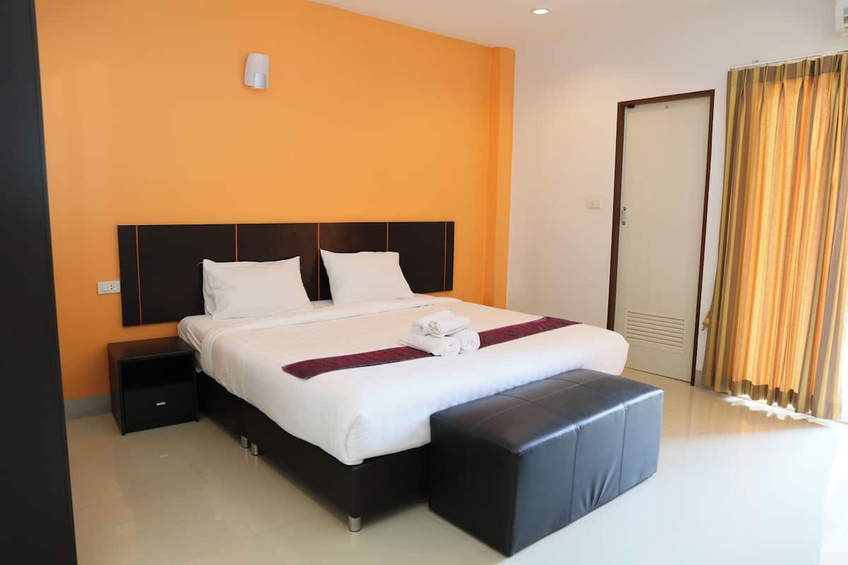 Une chambre d’hôtel avec un grand lit, une table de chevet, un banc et une porte avec des rideaux.