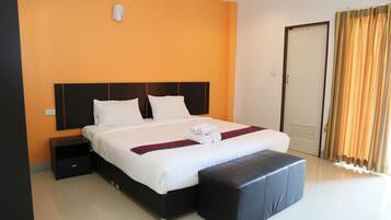 A hotel room with a large bed, a nightstand, a bench, and a door with curtains.