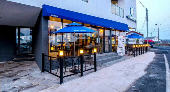 A coffee shop with outdoor seating and a blue awning.