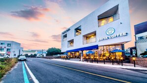 A modern building with a coffee shop named 'EDIYA COFFEE' on the ground floor. There are outdoor seating areas with umbrellas. - Blanc Bleu Pension (Seogwipo)