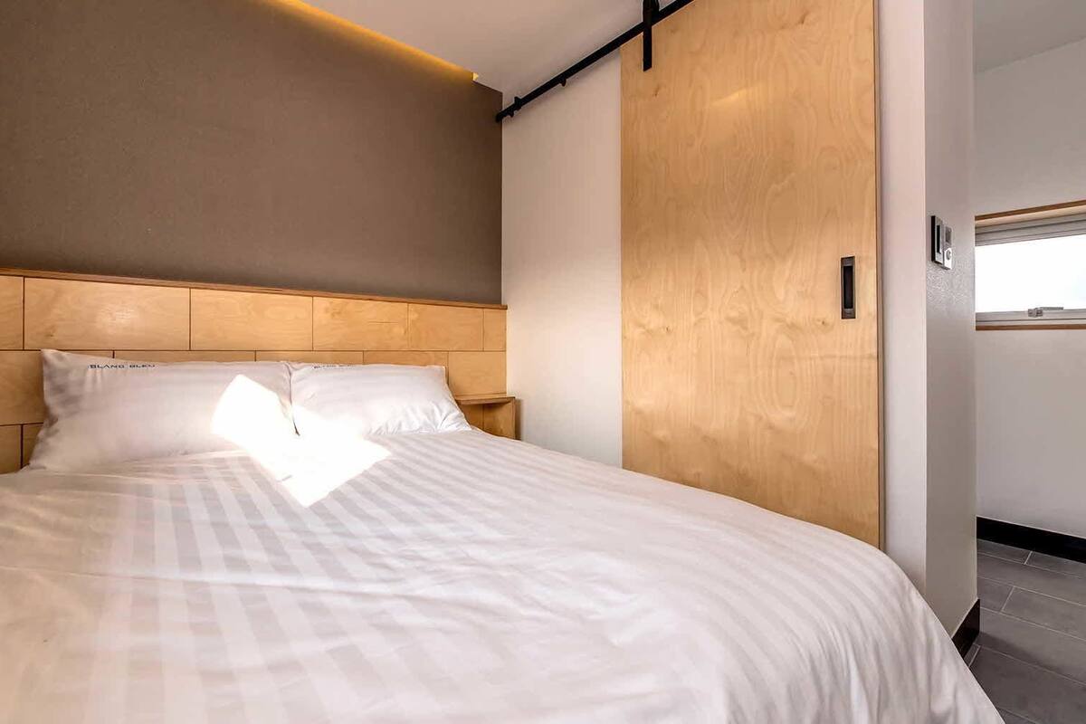 A modern hotel room with a large bed, wooden headboard, and a view of the sky through a window.