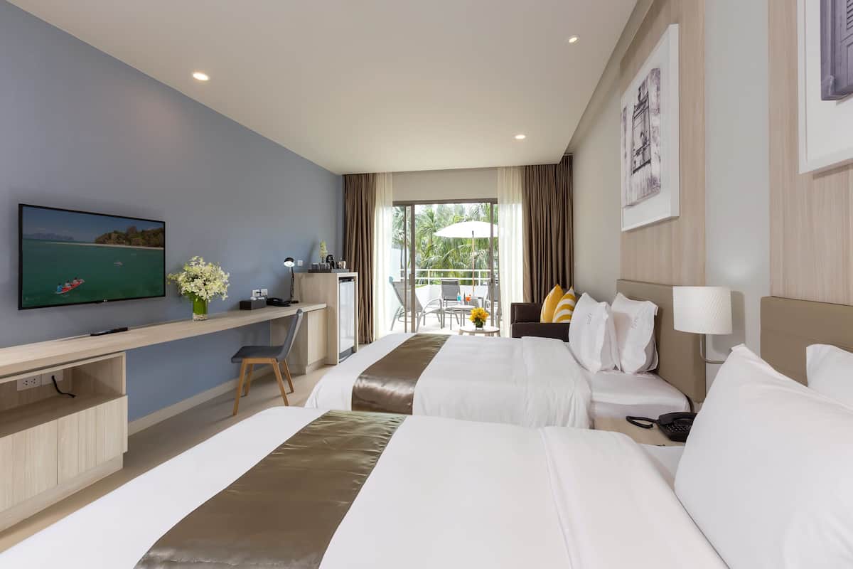 Quarto de hotel com duas camas, uma escrivaninha, televisão e varanda com mesa e cadeiras.