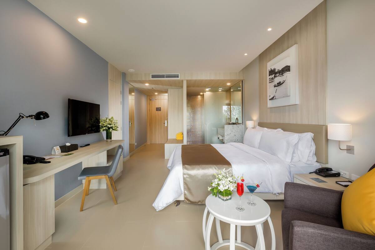 Quarto de hotel moderno com cama, escrivaninha, cadeira e uma pequena mesa com bebida.