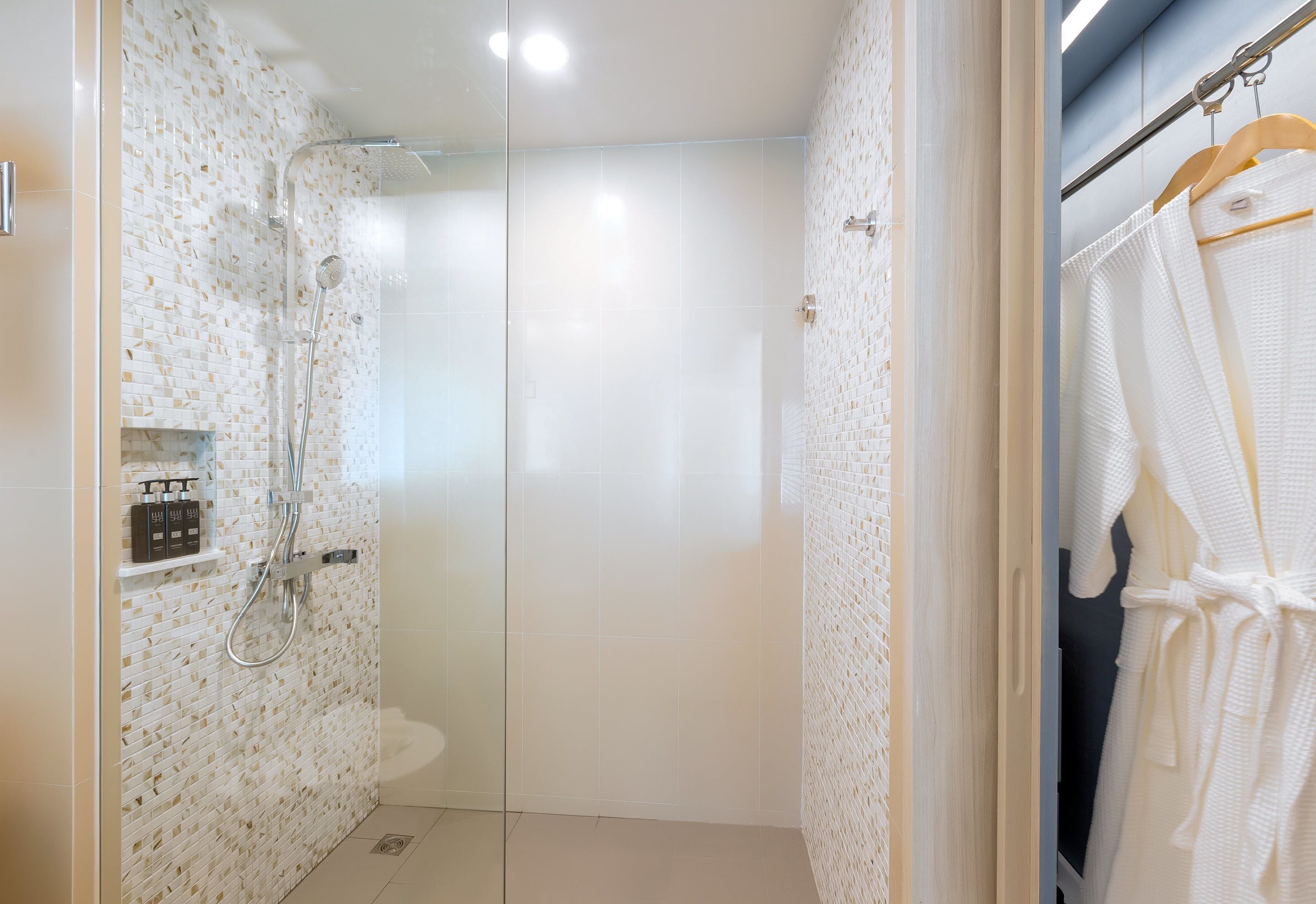 A modern bathroom with a glass shower enclosure, a white tiled wall, and a wooden door.