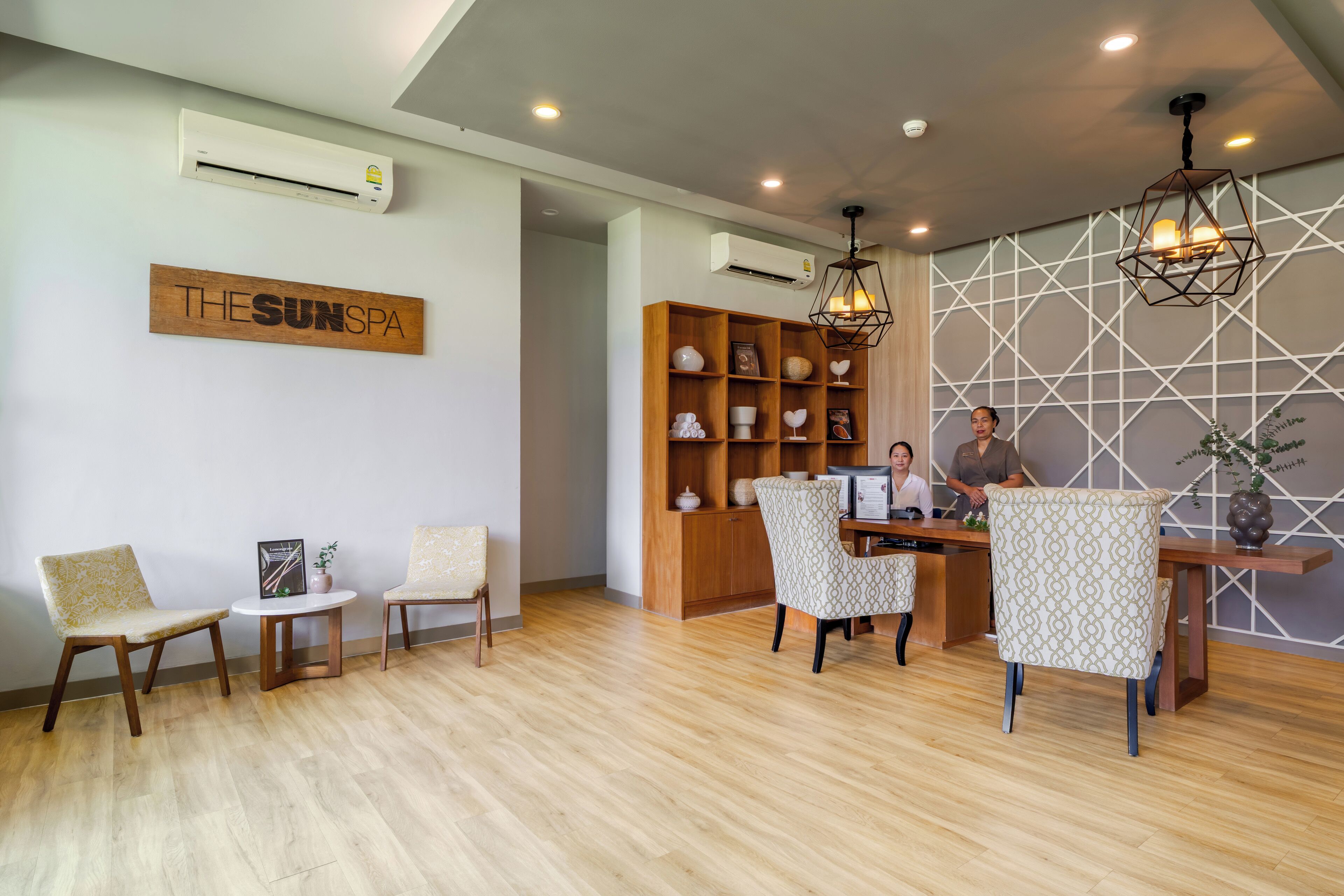 A reception area with a wooden reception desk, two receptionists, a wooden wall with a geometric pattern, and a sign that reads 'THE SUN SPA'.