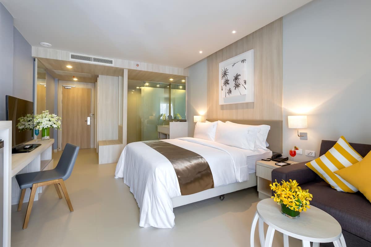 Quarto de hotel moderno com cama grande, escrivaninha e área de estar.