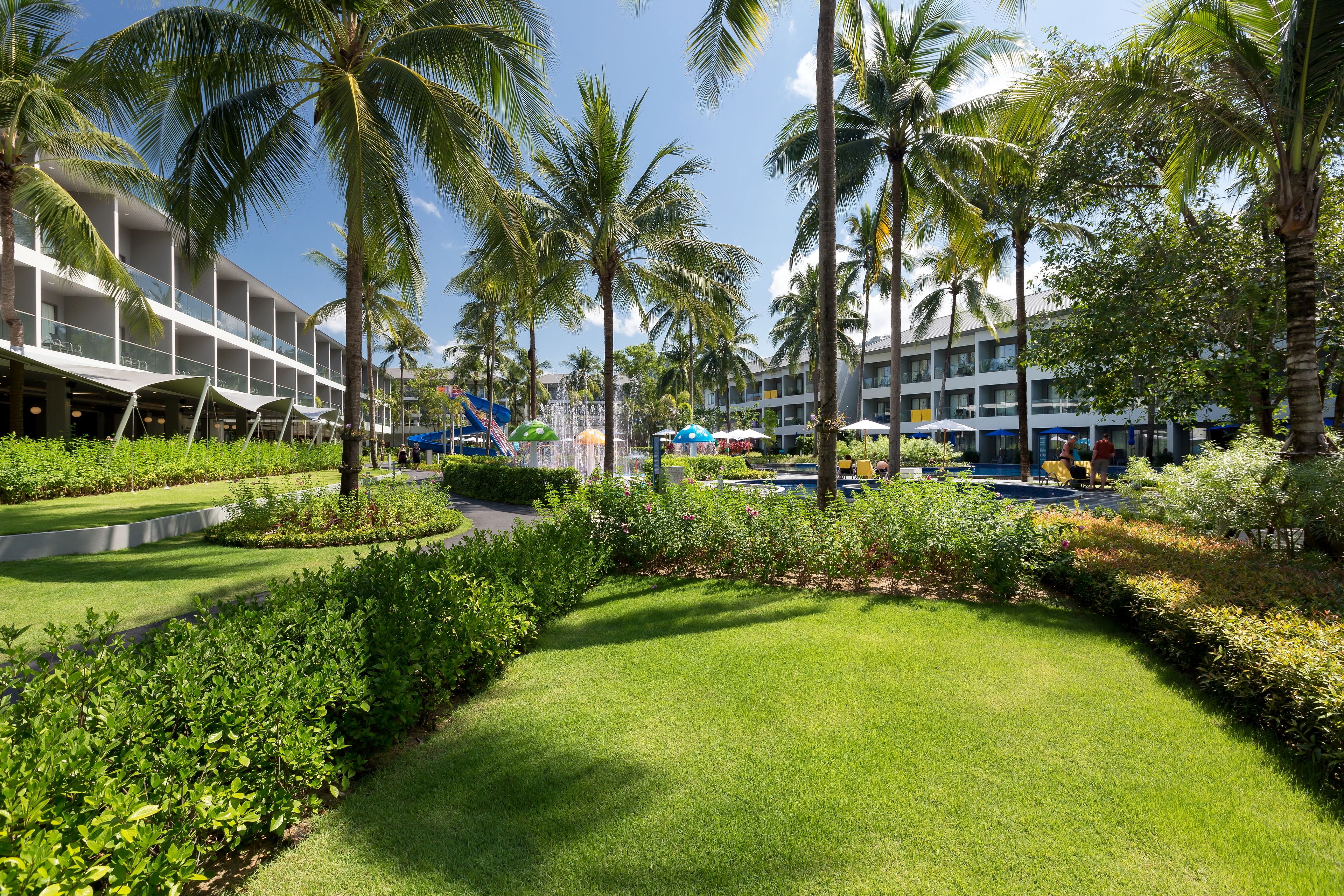Ein Resort mit gepflegtem Rasen, Palmen und einem Poolbereich mit Sonnenschirmen.