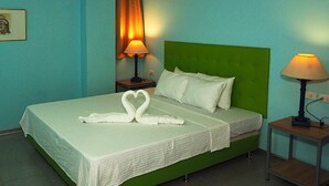A hotel room with a green headboard, two bedside lamps, a bed with white linens, and a heart-shaped towel arrangement. - New Era Mandaue Budget Hotel (Mandaue)