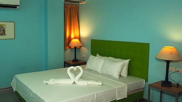 A hotel room with a green headboard, two bedside lamps, a bed with white linens, and a heart-shaped towel arrangement.