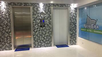 A lobby with mosaic tile walls, two elevators, and a 'New Era Budget Hotel' sign.