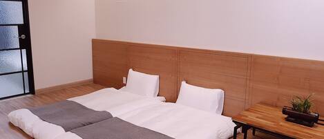 Una cama bien hecha con ropa de cama blanca y gris, un cabecero de madera y una mesita de noche con una planta.