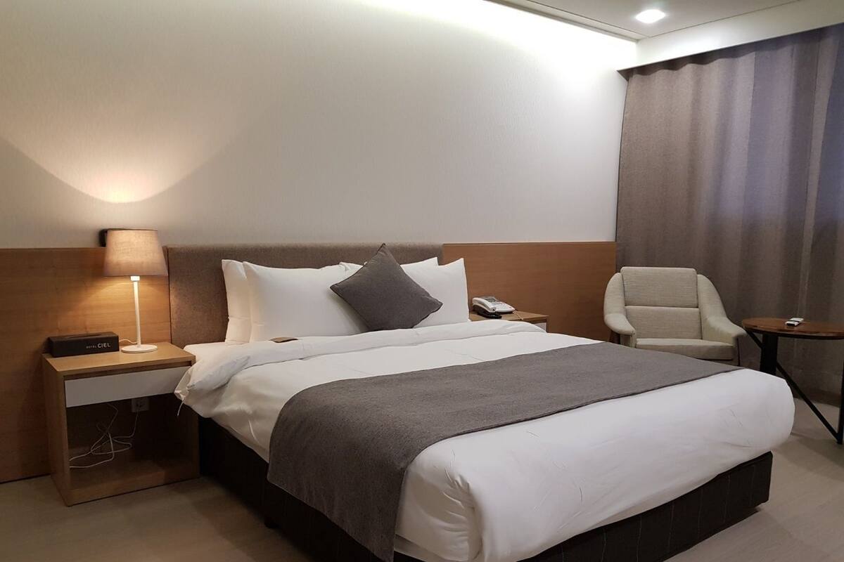 Ein Hotelzimmer mit einem großen Bett, einem Nachttisch mit Lampe, einem Sessel und einem kleinen Tisch.