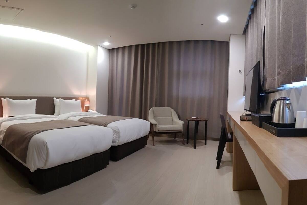 Ein Hotelzimmer mit zwei Betten, einem Schreibtisch, einem Stuhl, einem Fernseher und einer Kaffeemaschine.