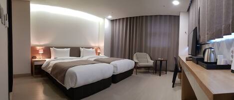 A hotel room with two beds, a desk, a chair, a TV, and a coffee maker.