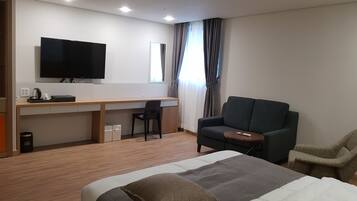 A hotel room with a bed, a desk, a chair, a sofa, a TV, and a window with curtains.
