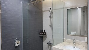 Ett modernt badrum med en duschavdelning med glasväggar, en tvättställ med en bänkskiva i marmor och hygienartiklar på en hylla.