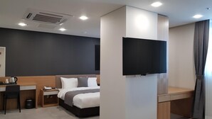 Ett modernt hotellrum med en säng, ett skrivbord och en platt-TV som är monterad på väggen.