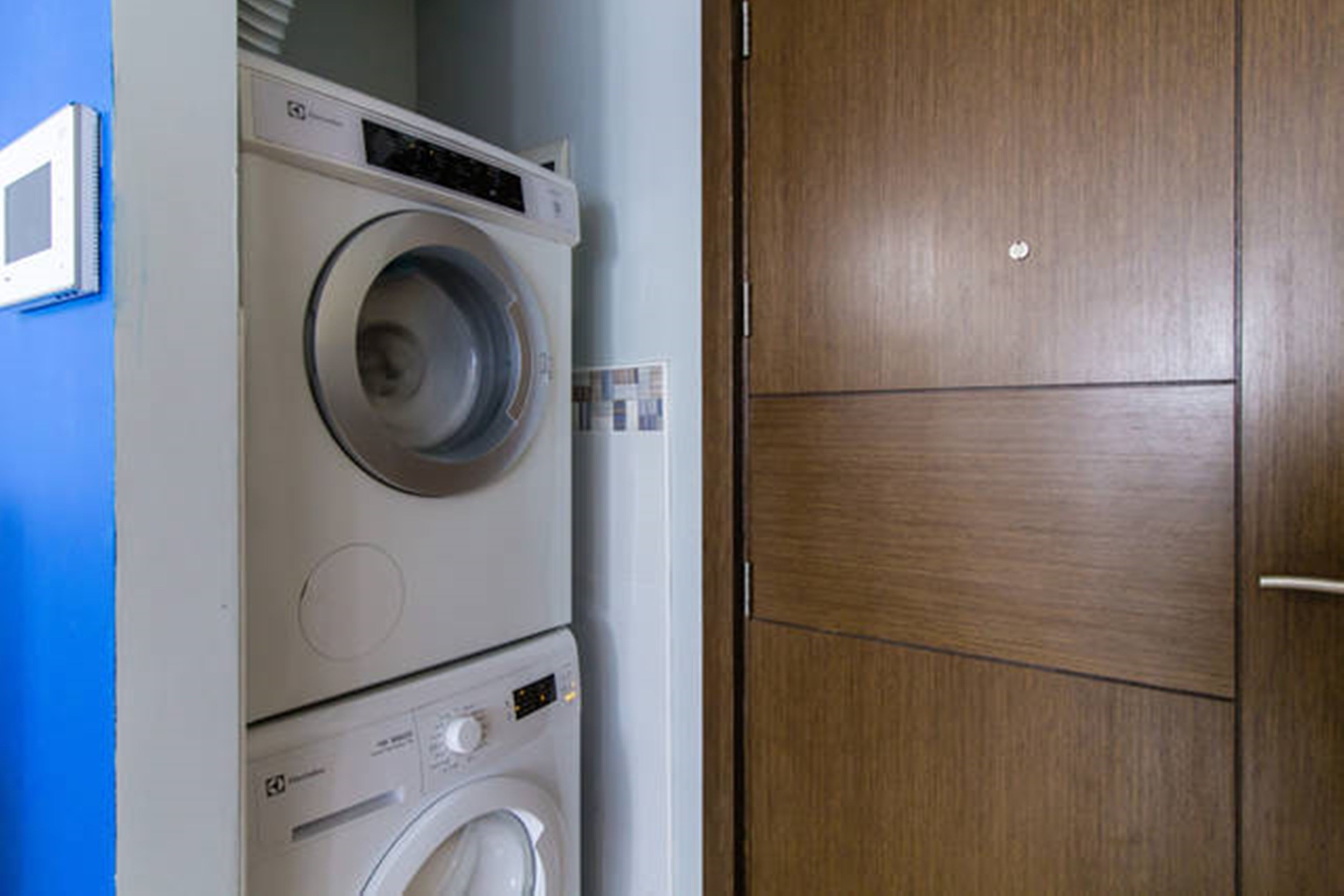 A stacked washer and dryer unit in a room with a wooden door and a blue wall.