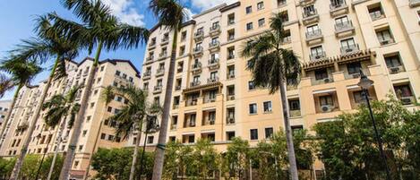 A multi-story residential building with balconies, palm trees, and a clear sky.