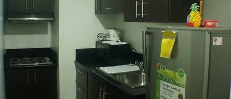 A compact kitchen with dark cabinets, a stainless steel refrigerator, and a microwave.