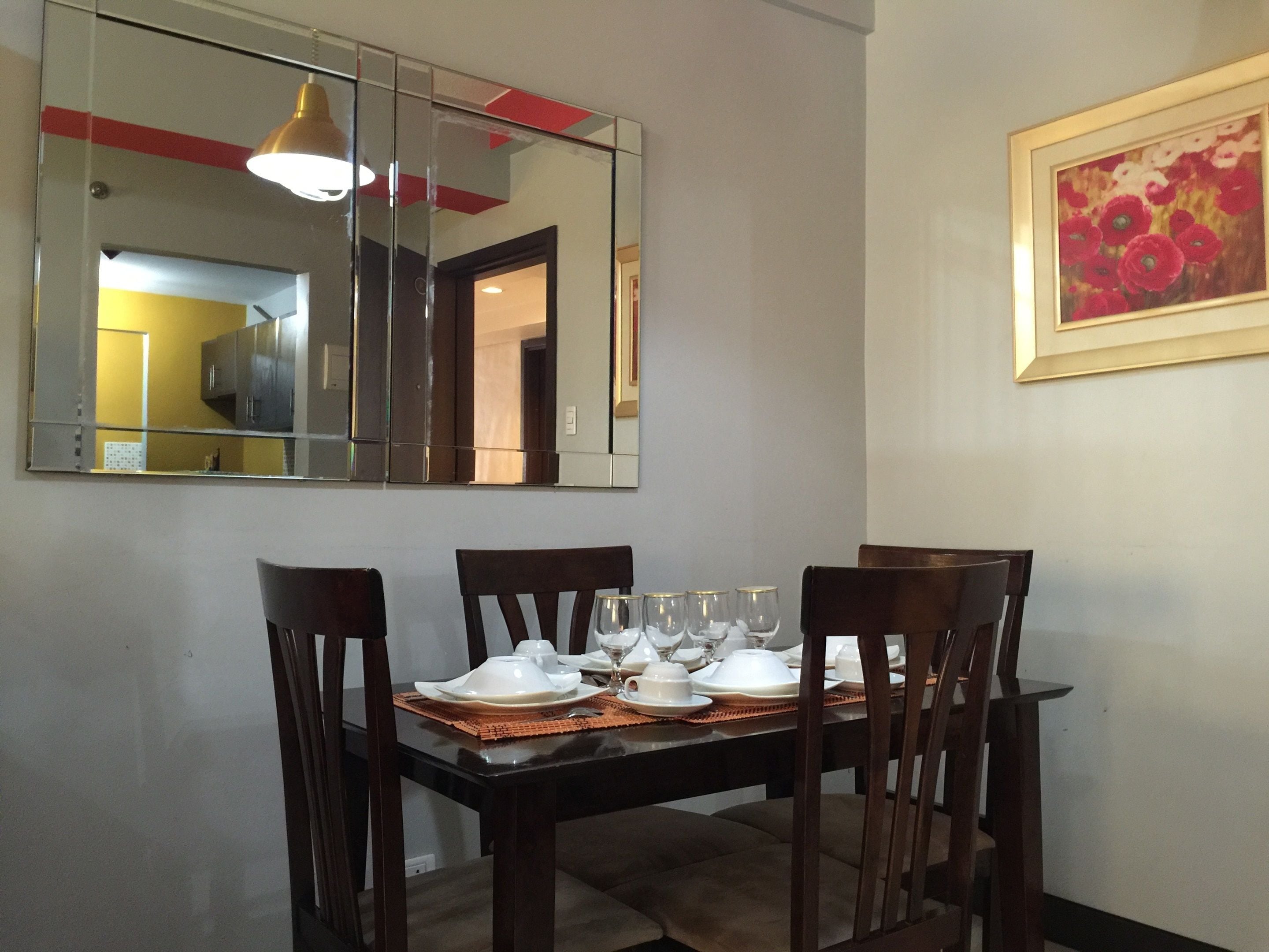 A dining area with a table set for four, a large mirror above the table, and a framed painting on the wall.