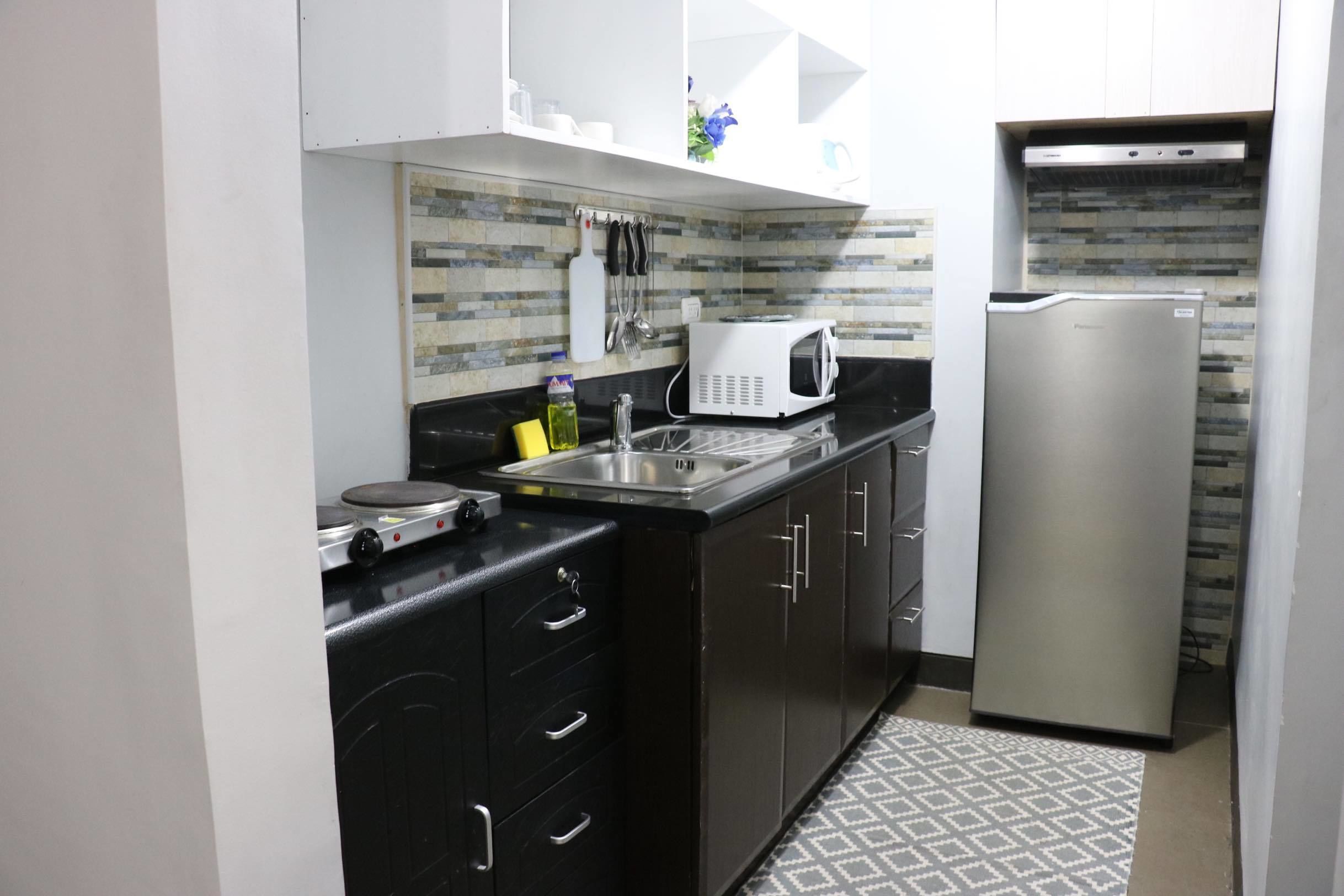 A compact kitchen with black cabinets, a stainless steel refrigerator, a microwave, and a tiled backsplash.