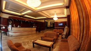 A lobby with a reception desk, seating area, chandeliers, and a television screen. - Rathna Residency (Coimbatore)