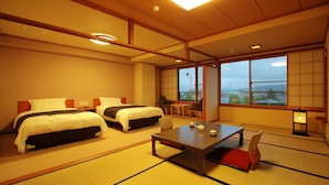 A traditional Japanese-style hotel room with tatami flooring, two beds, a dining table, and a view of the cityscape. - Asama Onsen Izumiso (Matsumoto)