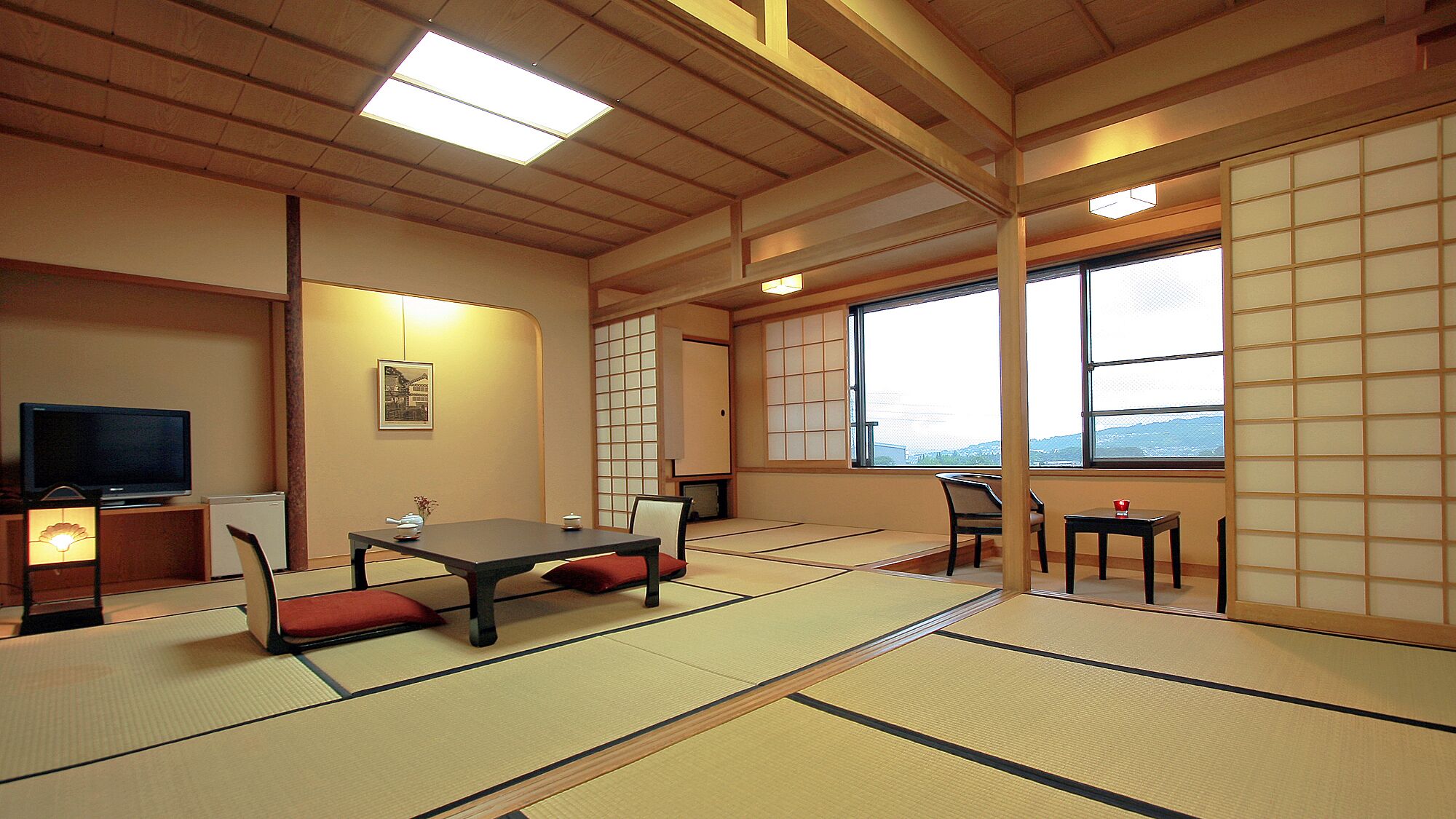 Une pièce de style japonais traditionnel, avec un sol recouvert de tatamis, une petite table basse avec des coussins, un téléviseur et une fenêtre donnant sur un beau paysage.