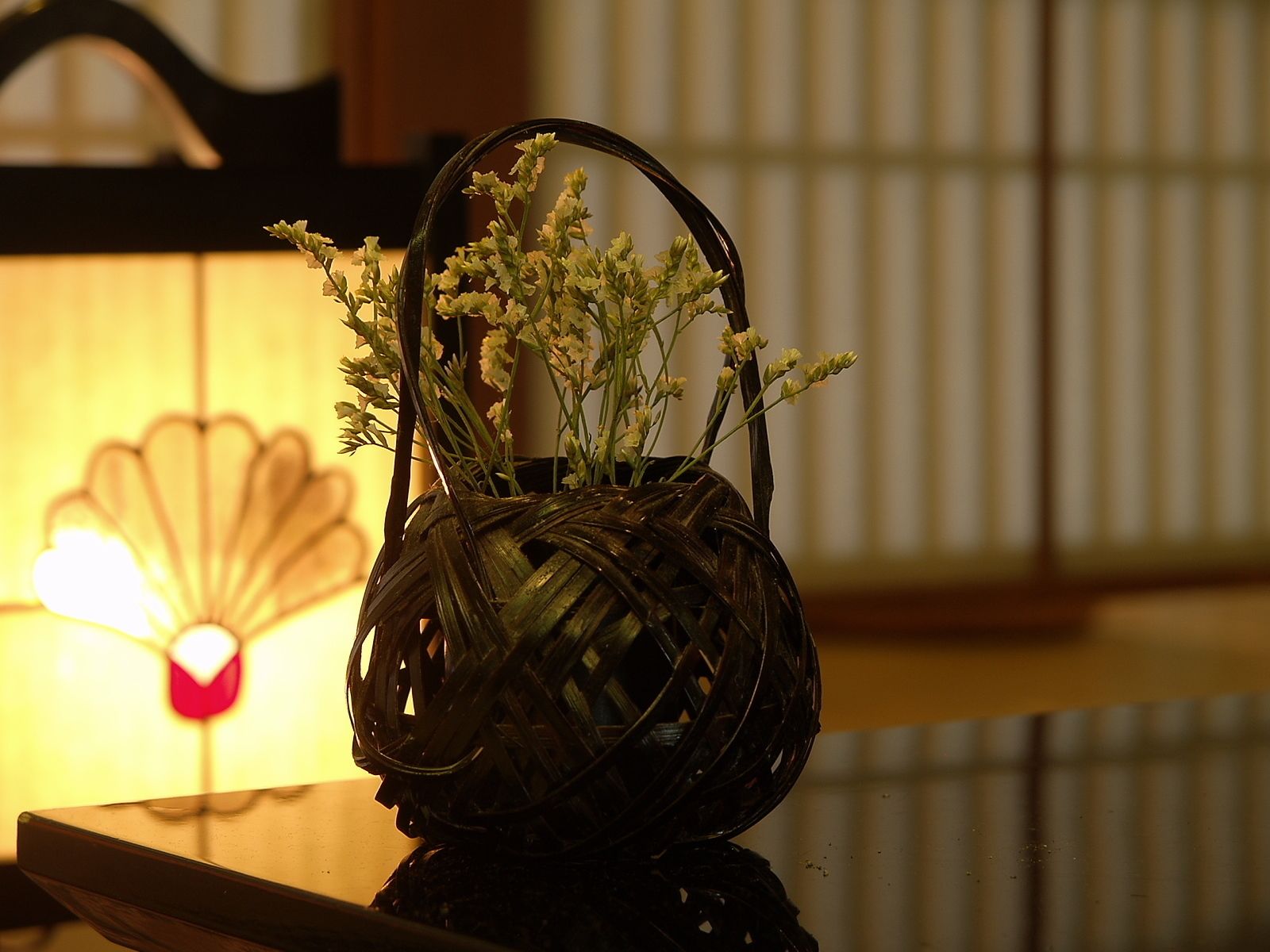 A woven basket with flowers on a reflective surface.