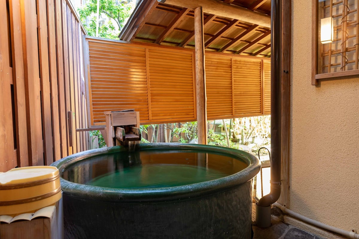 A traditional Japanese onsen with a wooden bath, a stone hot spring, and a bamboo-covered roof.