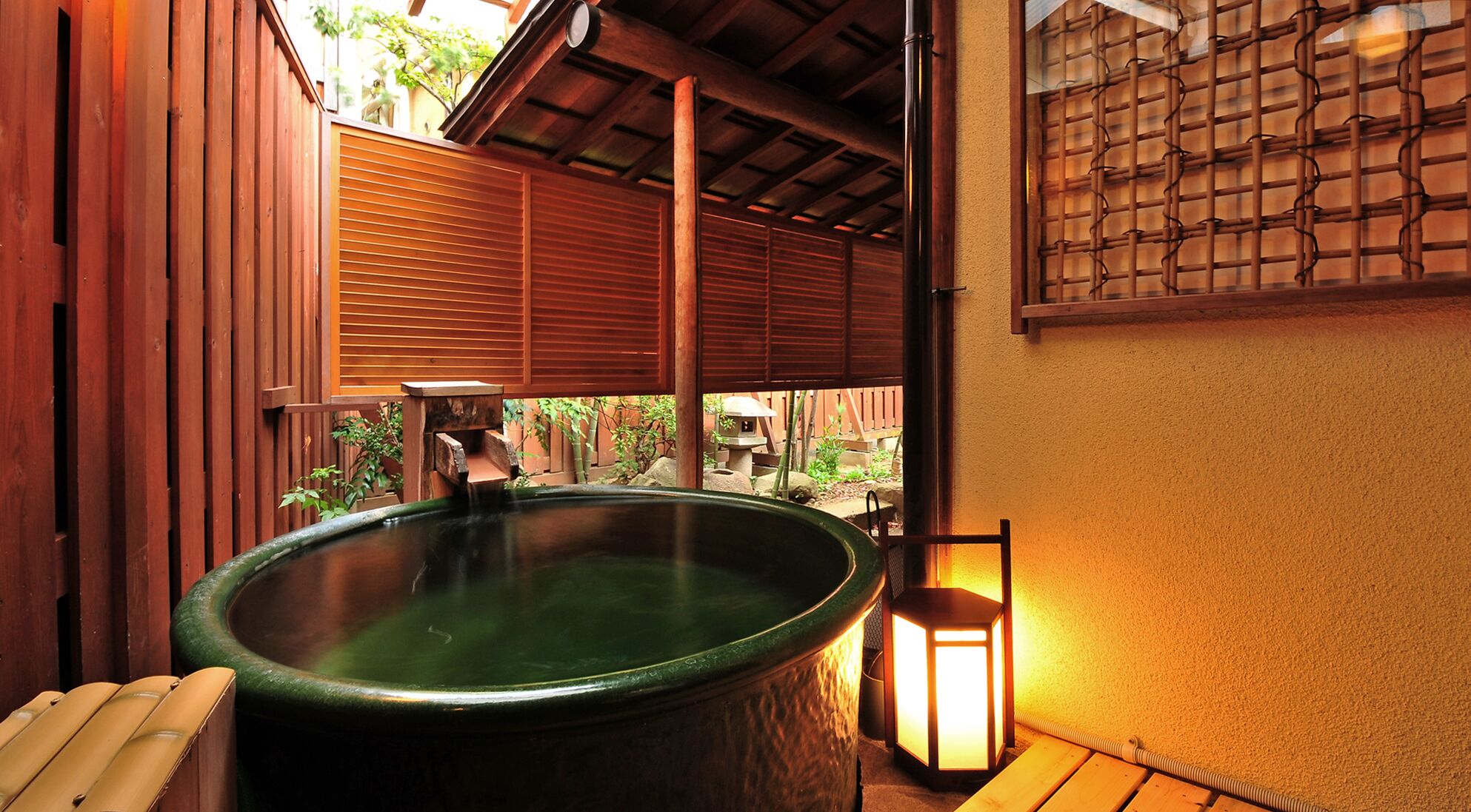 Un bain à remous avec une terrasse en bois, une lanterne et un paravent en bambou.