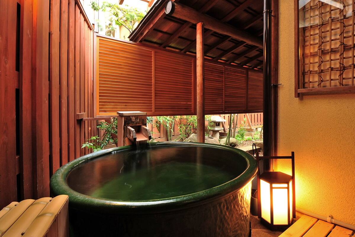 A hot tub with a wooden deck, a lantern, and a bamboo screen.