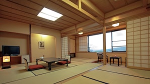 A traditional Japanese room with tatami flooring, a low table with cushions, a television, and a view through large windows. - Asama Onsen Izumiso (Matsumoto)