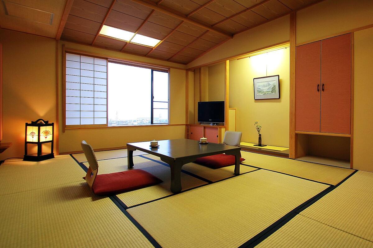 A tatami mat room with a low table, chairs, a television, and a cabinet.