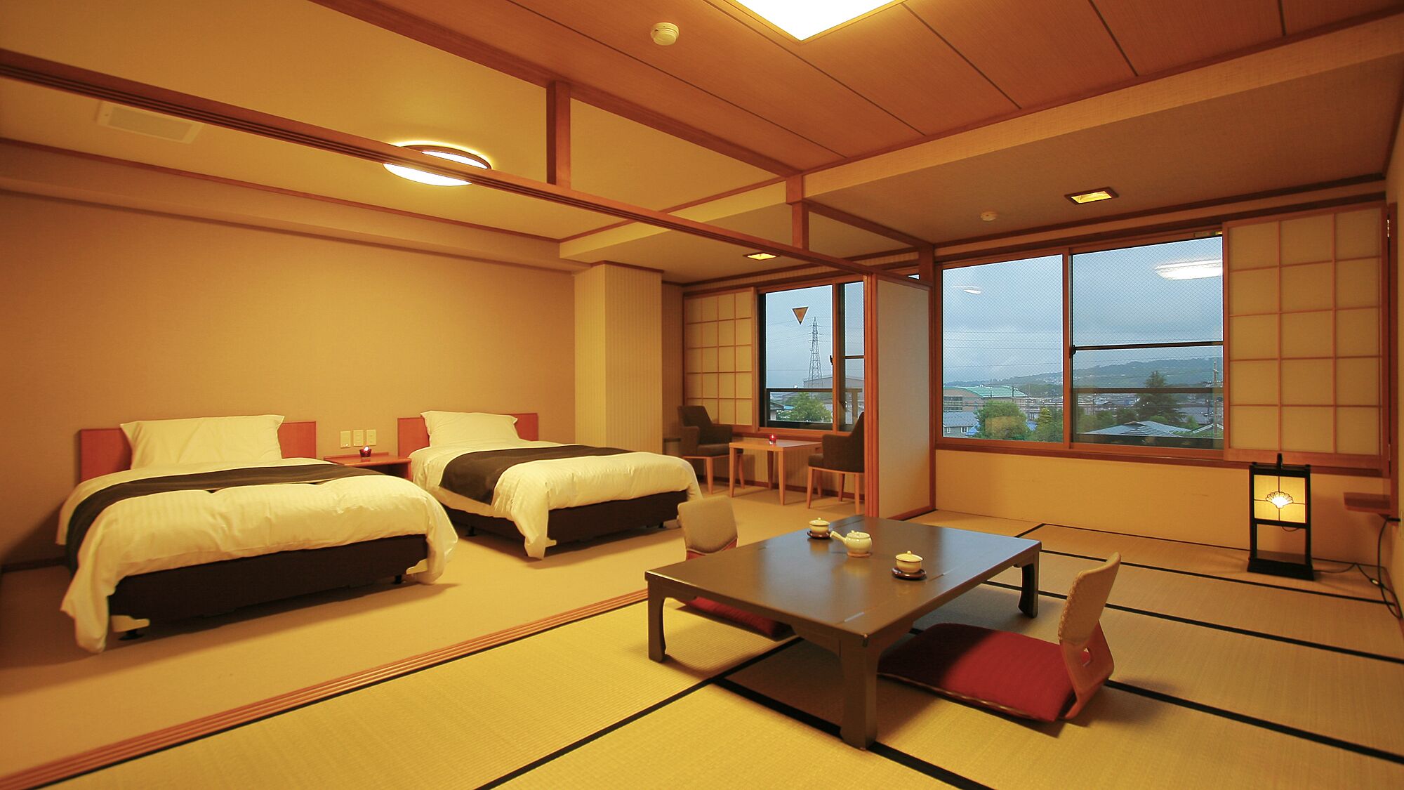 Une chambre d’hôtel avec deux lits, une petite table, une chaise et de grandes fenêtres donnant sur un beau paysage.