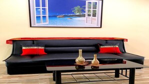 Un canapé noir avec des coussins rouges et deux vases posés sur une table basse en verre.