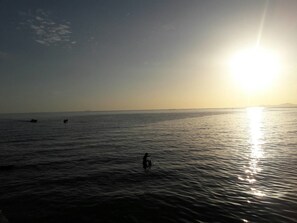 A calm sea at sunset with boats and a person in the water. - Breezy House Jomtien (Pattaya)