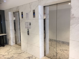 An elevator with marble walls and a floor, equipped with digital displays and an emergency exit sign.