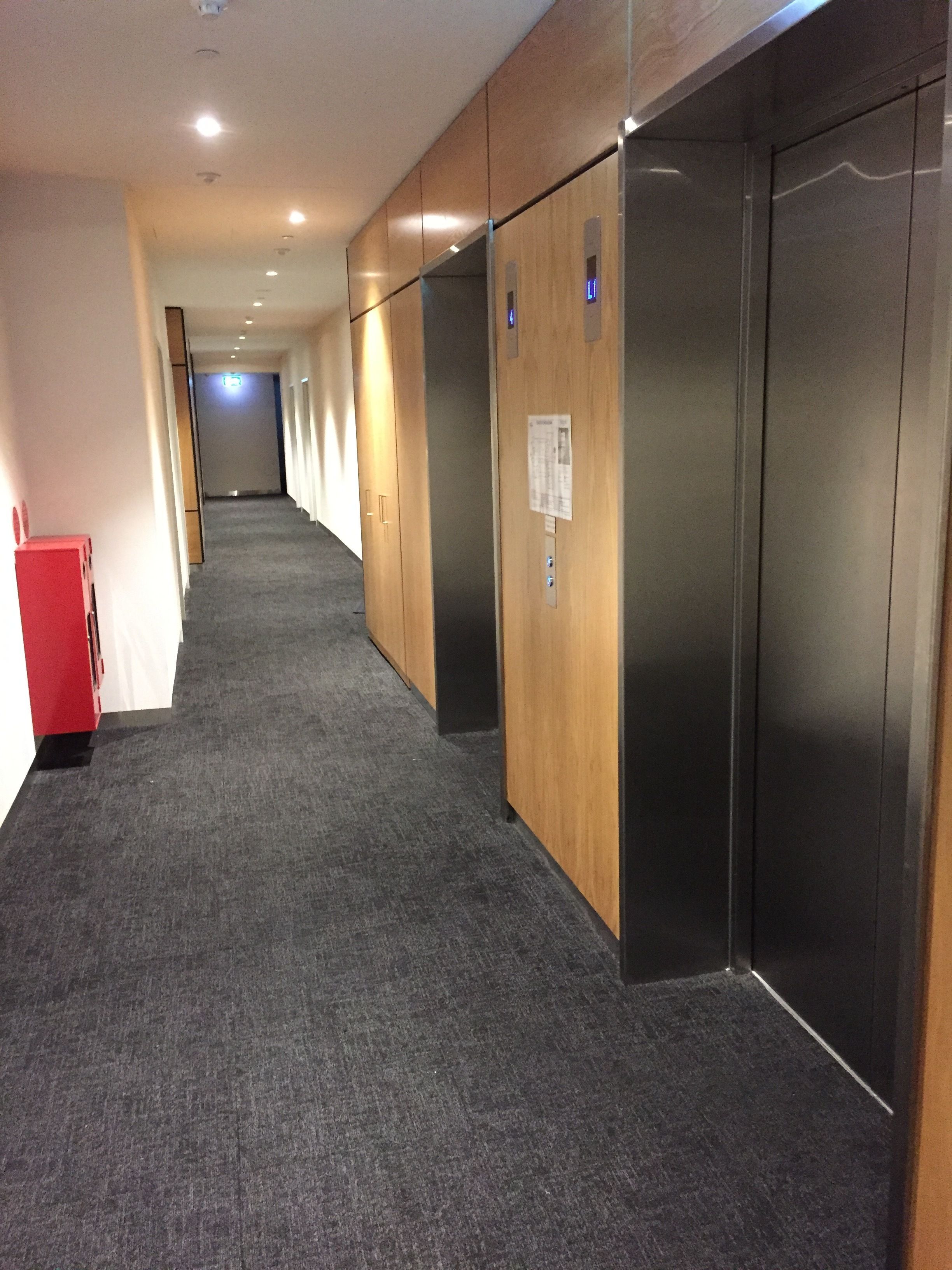 A hallway with carpeted floors, wooden walls, and two elevators.