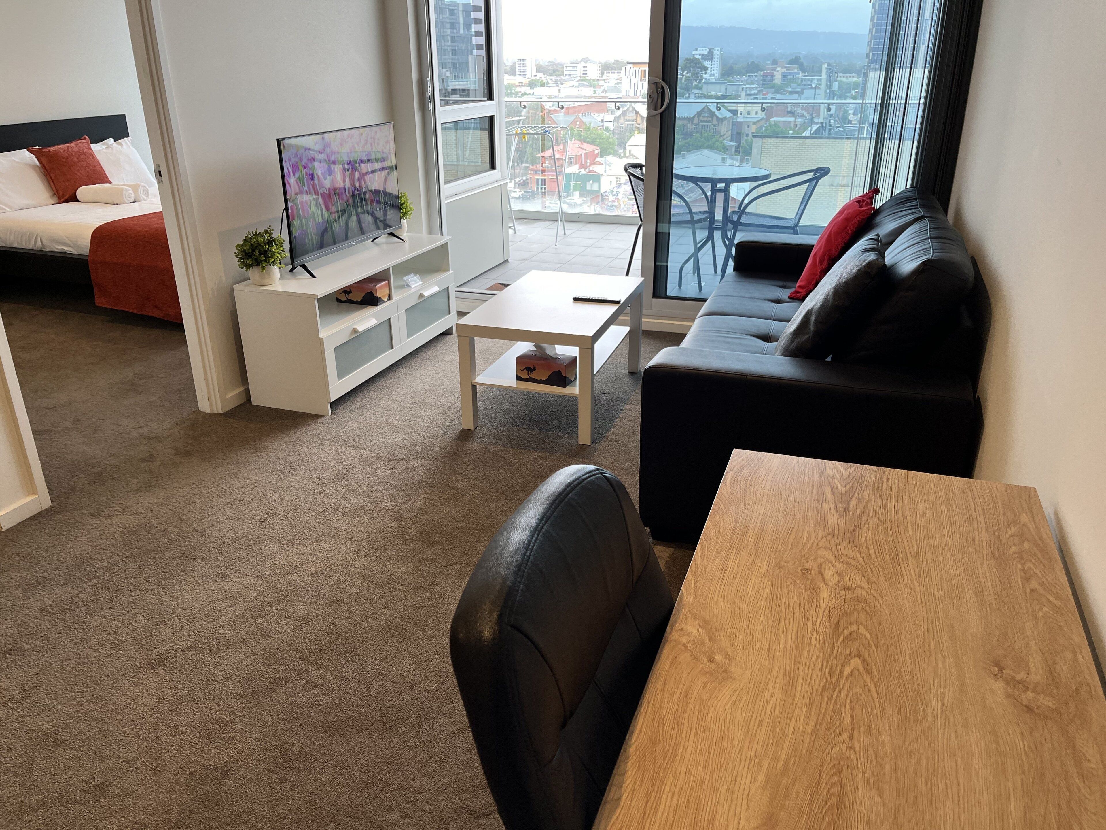 A modern living room with a sofa, a coffee table, a TV, and a balcony with a city view.