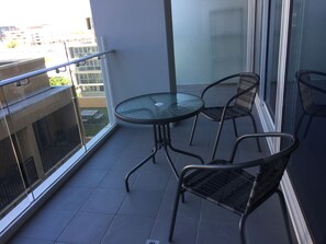 A balcony with a glass table and four chairs, overlooking a cityscape. - Tasha's Apartments on Morphett (Adelaide)